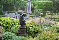 View from terrace: border of perennials, child angel statue, gardenhouse and decorative urn. Yvan and Gert garden In Belgium.
