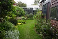 View looking from rear of garden towards back of the house, shows curved garden beds, a soft leaf buffalo lawn and a variety of flowering herbaceous plants.