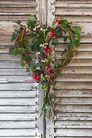 A rustic Valentine's wreath made with Hedera helix, Willow stems, Birch twigs, Cornus sanguinea 'Midwinter Fire', Tulip 'Rococo', Viburnum tinus and Chamelaucium