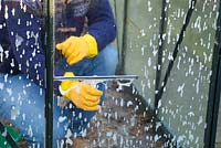Man cleaning dirty glass panes of a small patio greenhouse