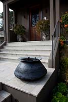 A black glossy cauldron style pot on a landing at the front entrance of a house