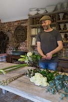A man constructing the winter bouquet with Rosa 'Avalanche', Viburnum tinus and Hippeastrum 'Christmas Gift'