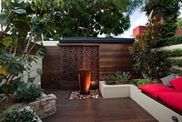 Inner city courtyard with raised beds including a Cercis tree. A water feature sits in front of a rusty decorative screen