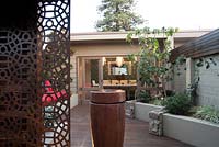 Inner city courtyard with a freestanding ceramic water feature, a rusty decorative screen, a raised garden bed,a raised garden bed with a combination of cement rendered and stacked stone wall, featuring a Cercis tree.