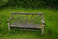 A garden bench amongst long grass of a wildflower meadow, Bluebell cottage garden Cheshire
