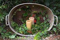 Arrangement in stainless steel basin containing Ilex aquifolium, Ivy, Pine cones, Juniperus and lit candles