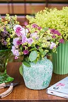 Bouquets of Astrantia major 'Ruby Wedding', Rosa 'Blush Noisette', Alchemilla mollis in green vases on the wooden work table by the fence. Katie's Lymphoedema Fund: Katie's Garden. Designers: Carolyn Dunster, Noemi Mercurelli, RHS Hampton Court Palace Flower Show 2016

