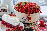 Redcurrants and strawberries in a bowl next to cake with meringue and silver cutlery