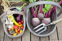 Wooden trug with freshly harvested summer vegetables, including tomatoes, onion, courgettes, aubergine, garlic and beetroot.