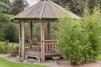 A bamboo gazebo with chairs set into gravel in an island bed.  Japanese style garden.  June, North Yorkshire. 