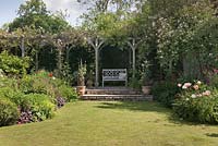 Cottage garden with rose covered pergola with painted pale blue bench. Cheshire, June. 