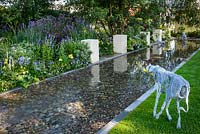 Wire dogs sculptures in a rectangular pool with pebbles and white blocks reflected in the water.  The Dog's Trust: 'It's a Dog's Life', Hampton Court Flower Show, July 2016