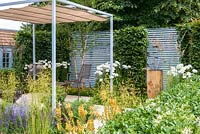 Steel pergola with canvas over a table and chairs on white paved raised terrace area, drought tolerant plants including verbascum, echinaceas, artemisia, geum, perovskia, stipa gigantea and salvias. Retreat Garden, RHS Hampton Court Flower Show in 2016