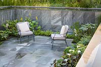 Sunken seating area with CED Natural stone Ebony Cloud Paving and two armchairs. Plants include Astilbe,'Sprite', Fatsia japonica 'Variegata, hostas and ligularia. Perennial Immerse Garden, RHS Hampton Court Flower Show 2016. Designed by Cherry Carmen