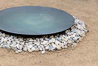 A round metal bowl water feature on a bed of pebbles.The Abbeyfield Society: a Breath of Fresh Air, RHS Hampton Court Palace Flower Show 2016.