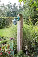 Wooden lamp post in a bed with Fuchsia, Miscanthus sinensis and Miscanthus sinensis 'Gracillimus'