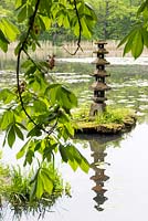 Oriental statue on its own tiny island, makes a focal point off the shoreline of the lake in the naturalistic Japanese area near the castle wall. Framed by Aesculus flava 'Vestita' - sweet buckeye, a member of the horse chestnut family.