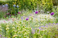 A section of a herbaceous border featuring contemporary metal garden ornaments at Bluebell Cottage Gardens. Plants include ornamental grasses, Phlomis russeliana, Lychnis coronaria, Papaver somniferum and Alliums