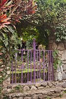 Purple painted decorative metal gate in stone wall dividing garden rooms - Lake Atitlan Hotel, Guatemala