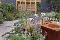 Rusty metal cubes amongst drought tolerant perennial planting and a wooden arbour seating area in patio garden - Coastal Retreat at RHS Tatton Park Flower Show 2016