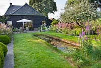View across the garden with natural pond, perennial borders and relaxing patio. Lythrum salicaria. Design: Karin Cruijs
