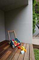 A childs play area under a set of stairs with a timber deck, timber children's toys next to grey painted cement rendered wall.