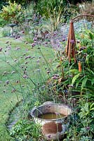 Little Ash Garden, Fenny Bridge, Devon. Metal bucket in autumn border with Verbena bonariense and metal sculptures