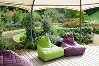Modern garden with decking and multi coloured soft cushion seats under gazebo Hawkley Cottage Gloucestershire. September