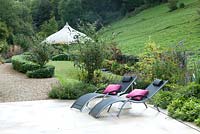 Sun loungers on patio with gravel path leading to gazebo in rural garden 