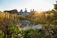 Sun setting in pub garden with raised beds, seating area with fire burner and late summer border. Jo Thompson garden design in Ticehurst, East Sussex