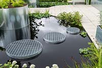 Contemporary water feature with metallic planters and grated steps across black water.