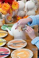 The second of six stencils is applied to the teapot, and more details of the flower are carefully applied.