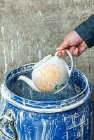 A biscuitware pottery teapot is dipped into a barrel of glaze so that it is thoroughly coated.