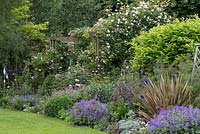 Rose pergola with Rosa 'Madame Alfred Carriere', 'Felicite Perpetue' and 'Coral Dawn'. In front, bed of hardy geranium, oriental poppy, phormium and foxglove.