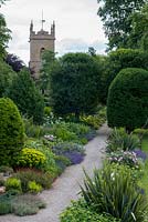 The Church Walk at Bretforton Manor with long double herbaceous borders and shaped yew trees.