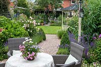 View from patio over table to  24m x 7.6m rear town garden. Lavender and box-edged pebble path leads past gazebo to circular lawn enclosed in cottage style herbaceous borders. At far end, there is shady seating, a compost bin amongst foxgloves, and greenhouse.