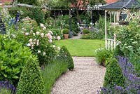 A 24m x 7.6m rear town garden. Lavender and box-edged pebble path leads past gazebo to circular lawn enclosed in cottage style herbaceous borders. At far end, there is shady seating, a compost bin amongst foxgloves, and work area