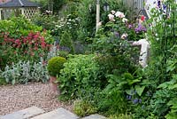 A patio is sheltered behind obelisk of sweet peas, roses and herbaceous planting, with a pebble path linking to the side gate and gazebo.