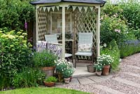 Overlooking the lawn and borders, a gazebo is flanked by pots of lavender and marguerites, hydrangeas and roses.
