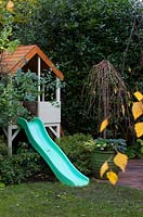 Children's slide and playhouse with potted Prunus 'Falling Stars'