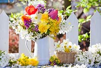 Display of spring flowers in jug. daffodils, tulips, mahonia, lunaria and cherry blossom branches.
