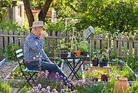 Man relaxing with cup of tea in spring vegetable and herb garden.
