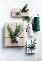 Wrapped presents using brown paper and string with reels of string, decorated with greenery from fir tree foliage and yew tree with half dipped pine cones