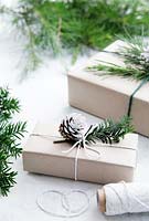 Wrapped presents using brown paper and string with reels of string, decorated with greenery from fir tree, yew tree and silvery foliage with half dipped pine cones