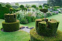 Topiary castles complete with flags overlook the herbaceous borders. Felley Priory, Underwood, Notts, UK