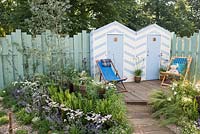 Blue and white painted beach huts with deck chairs on decking, Eucalyptus gunnii 'Azura' underplanted with Achillea millefolium 'Wonderful Wampee', Nepeta racemosa 'Walker's Low' - By The Sea, RHS Hampton Court Palace Flower Show 2017