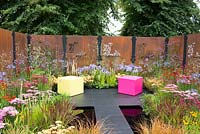 Decorative rusted steel panels enclose a colourful garden with pink and lime green cubed seating, plants include Helenium 'Moerheim Beauty', Penstemon 'Garnet', Agapanthus 'Blue Triumphator', Verbena bonariensis, Achillea 'Pretty Belinda', Achillea 'New Vintage Red' and Imperata cylindrica 'Rubra'- Colour Box, RHS Hampton Court Palace Flower Show 2017