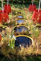 Kinetica garden. Young Betula trees planted in moving Kinetic planters placed amongst circular shallow pools surrounded with Anemanthele lessoniana Design: John Warland, Sponsors: Paneltech Systems. RHS Hampton Court Palace Flower Show 2017