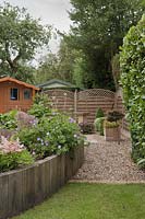 Corner of garden with upright railway sleepers creating raised beds next to evergreen hedge and fence - June, Summerfield Place, Cheshire