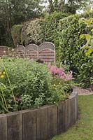 Garden with upright railway sleepers creating raised beds next to evergreen hedge - June, Summerfield Place, Cheshire